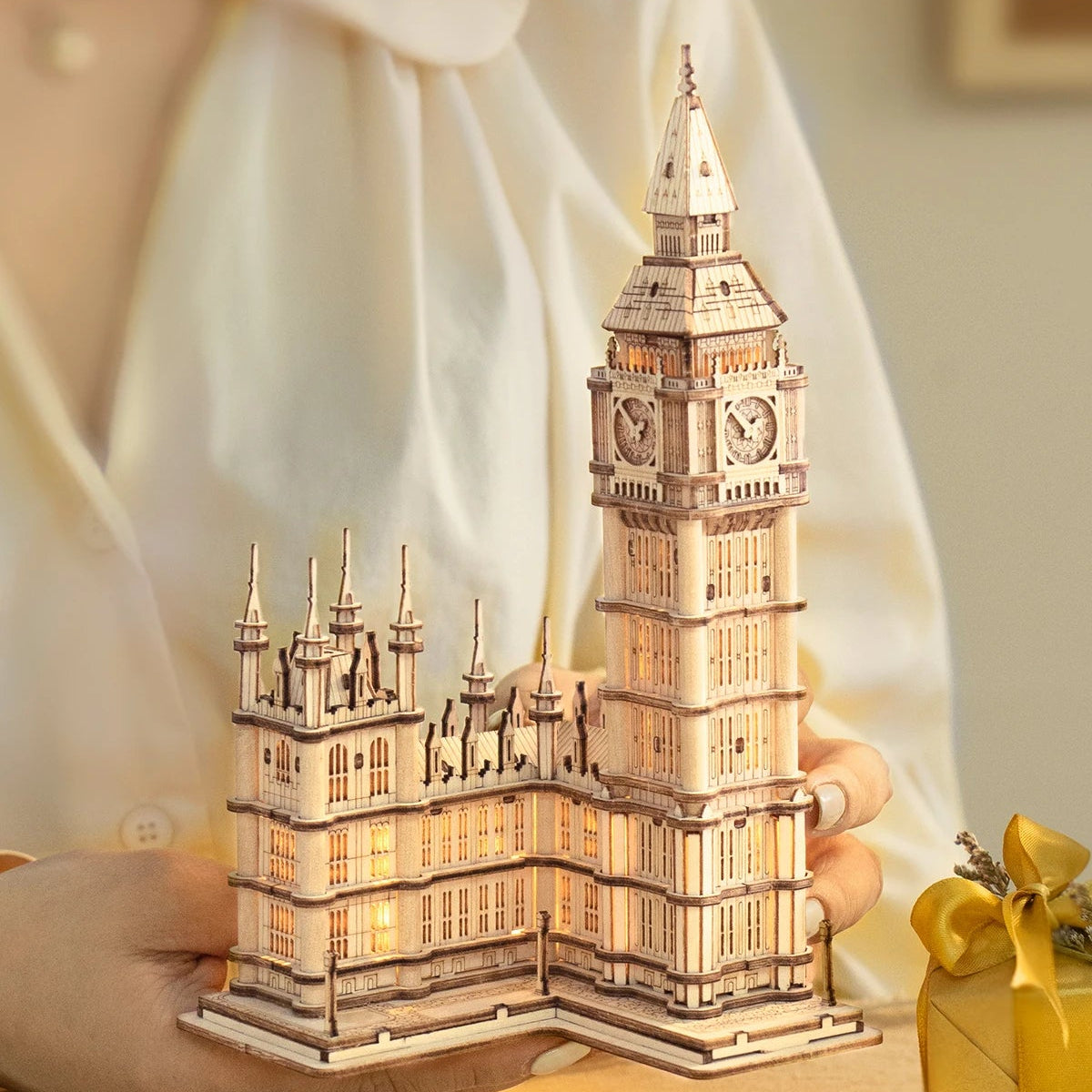 Hands holding the completed Big Ben wooden model beside a wrapped gift.