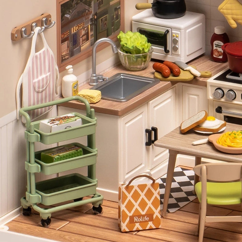A silver-colored sink and cream cupboards beside a green cart.