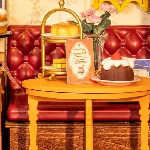 A tiered cake stand and tiny menu face the red buttoned bench.