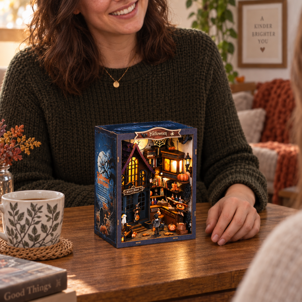 Generated display illustration of the completed Halloween book nook at approximately20cm tall beside an adult hand and mug