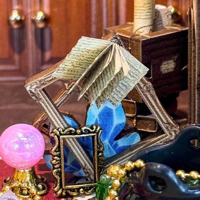 An open spellbook rises above a blue crystal and little mirrors.