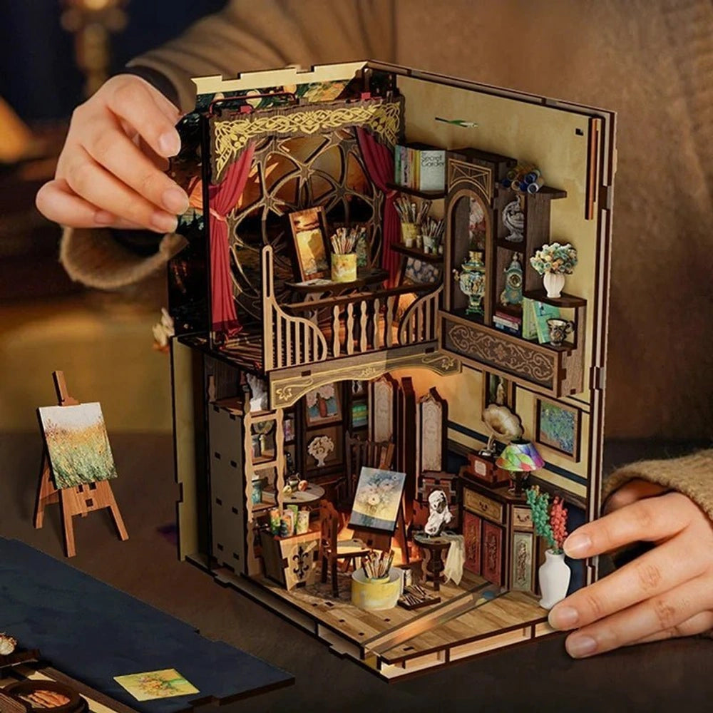 Hands open the finished World in a Frame miniature artist studio to reveal its paintings and furnishings