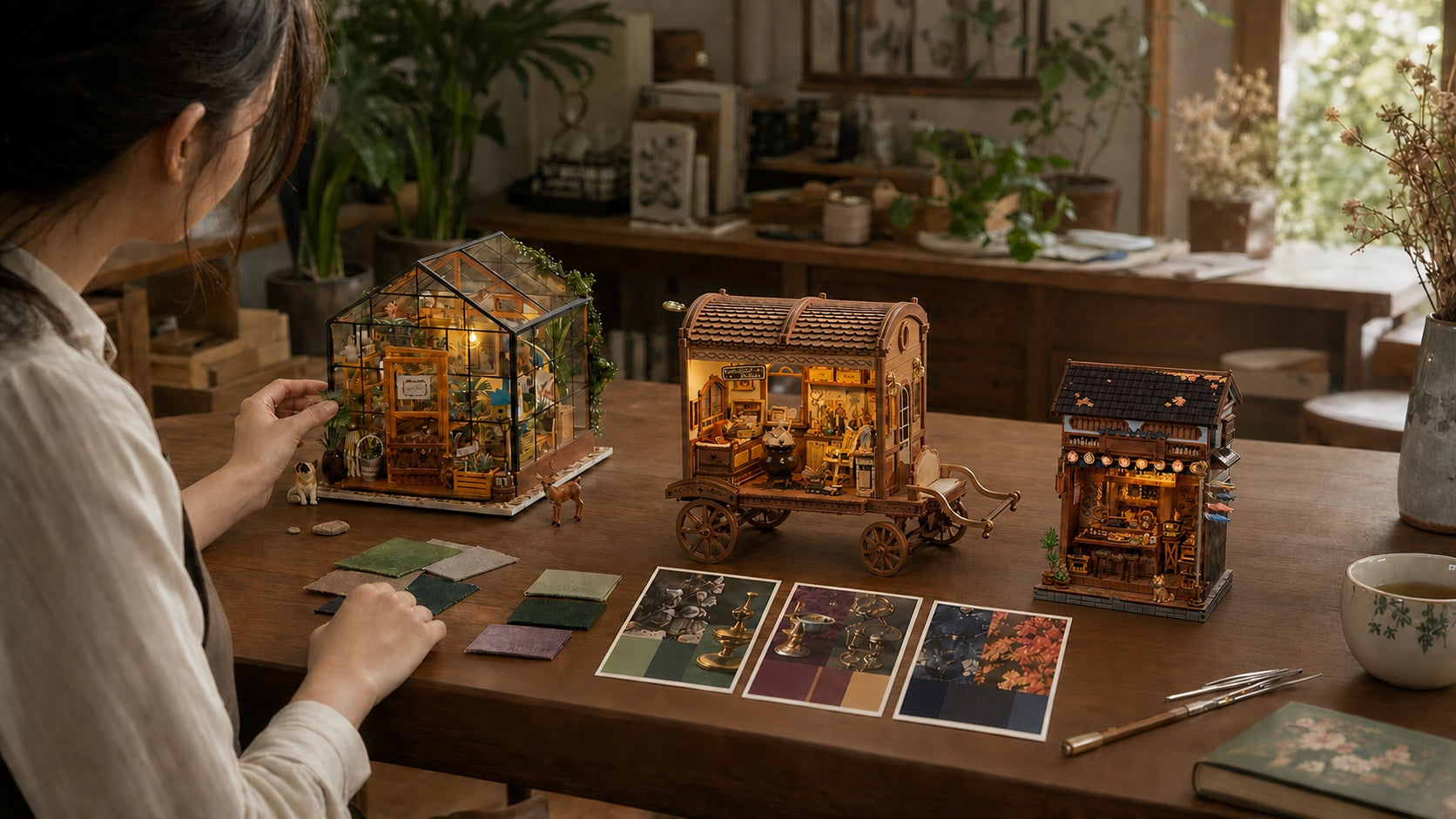 A maker comparing Cathy's Flower House, Wandering Wizard's Wagon, and Old Town Choshi miniatures on a craft table