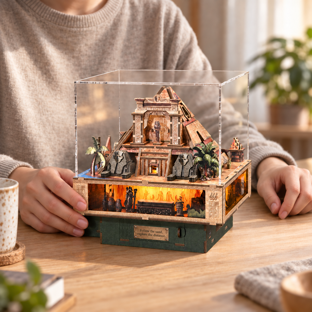 An adult maker with a completed Desert Secret Journey pyramid miniature on a wooden table at home.