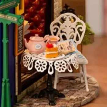 A pink teapot and a little cake wait beside the white chair.