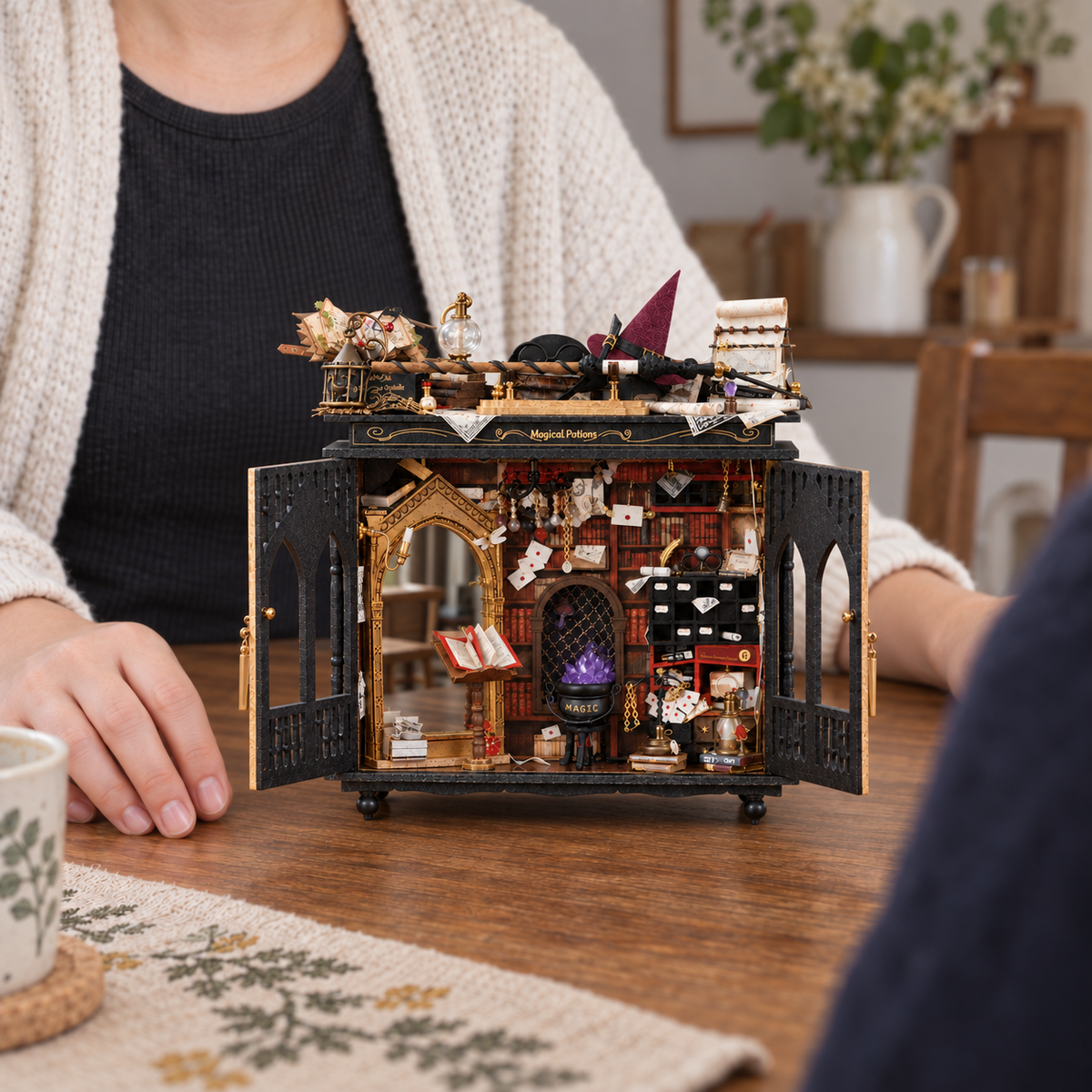 Completed Starspell Cabinet miniature workshop on a craft table beside adult hands, with lights off
